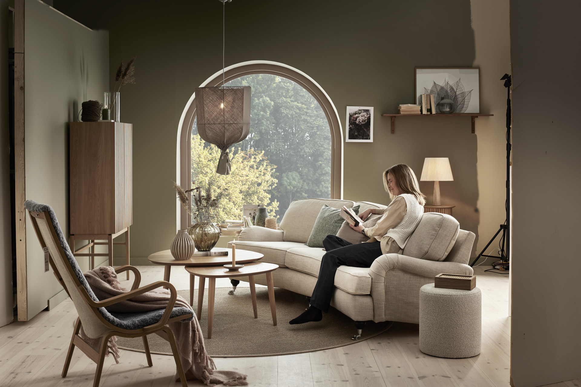I ett grönt vardagsrum sitter en kvinna och läser i en beige Oxford soffa
