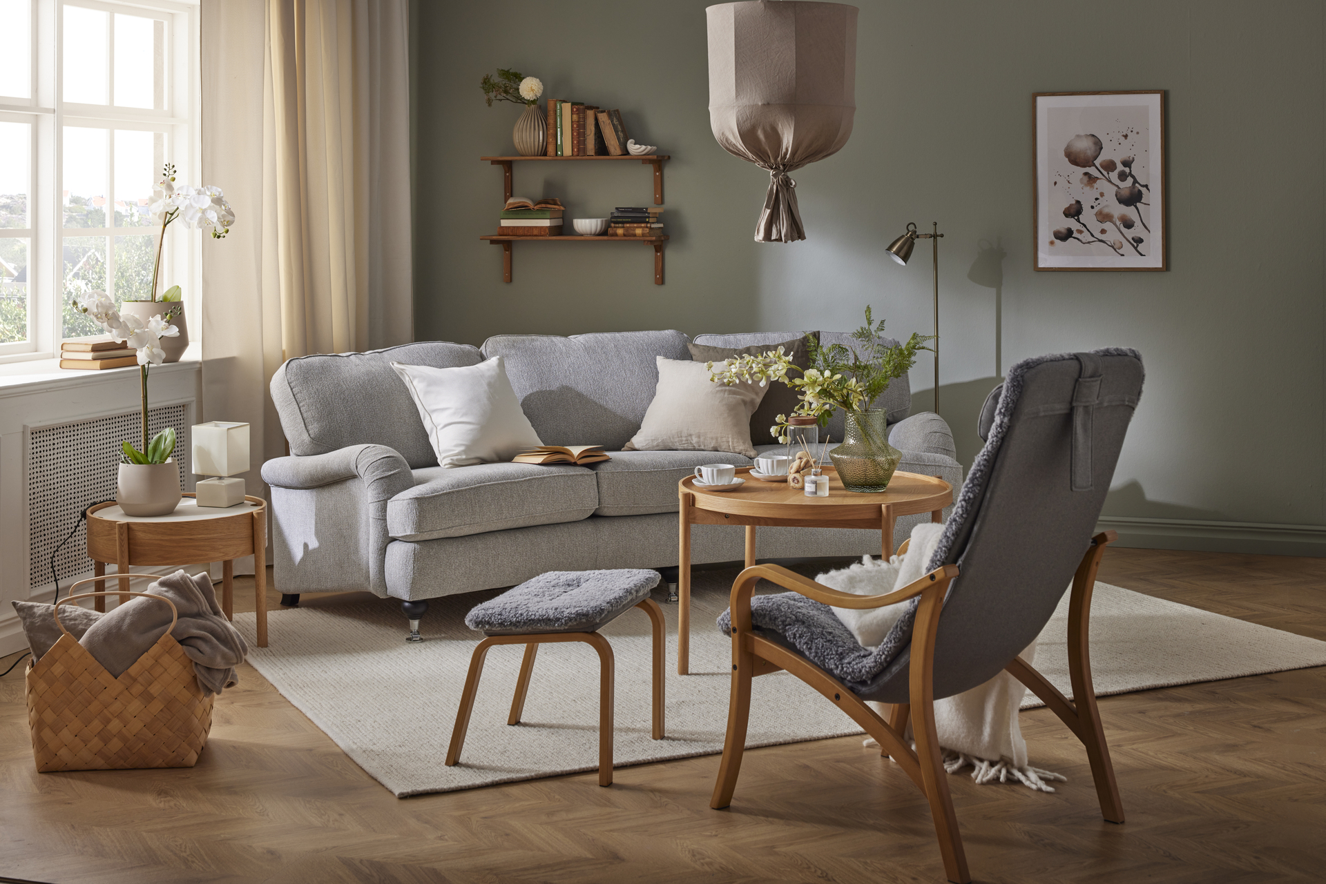 I ett grönt vardagsrum står en grå, svängd Oxford soffa