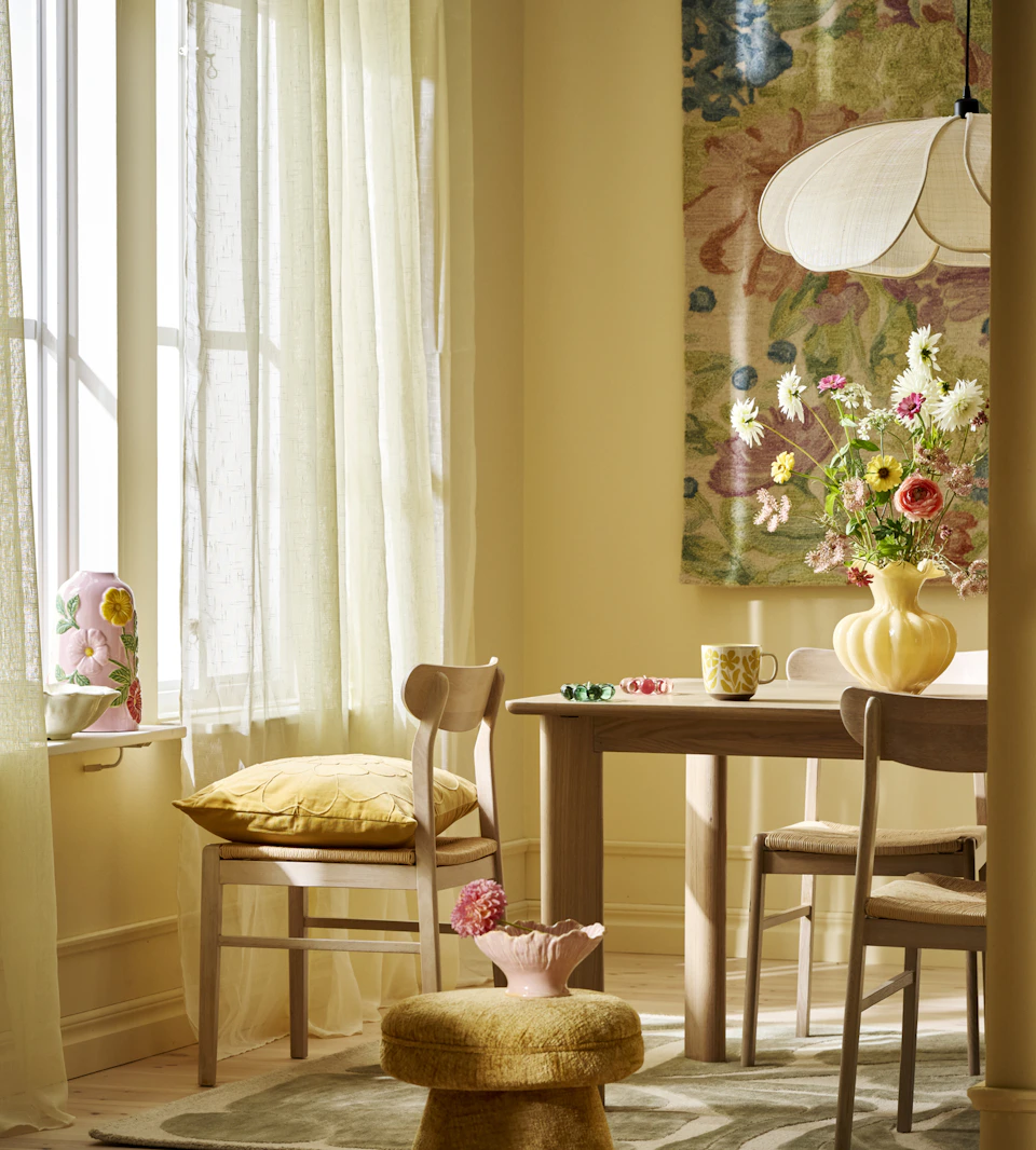 En matgrupp i ljust trä står i ett ljust matrum med gula väggar.