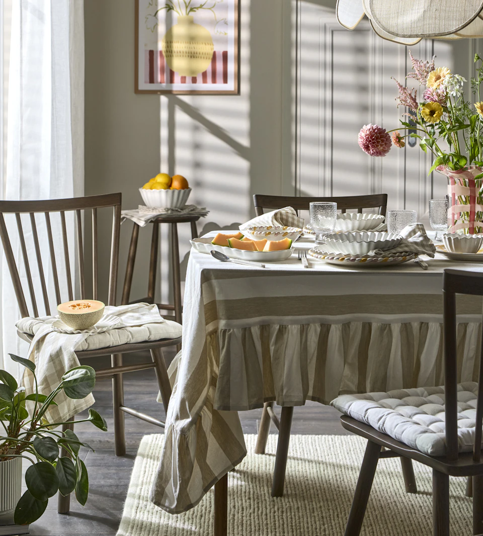 En matgrupp i mörkt trä är dukat med en randig duk och ljust porslin.