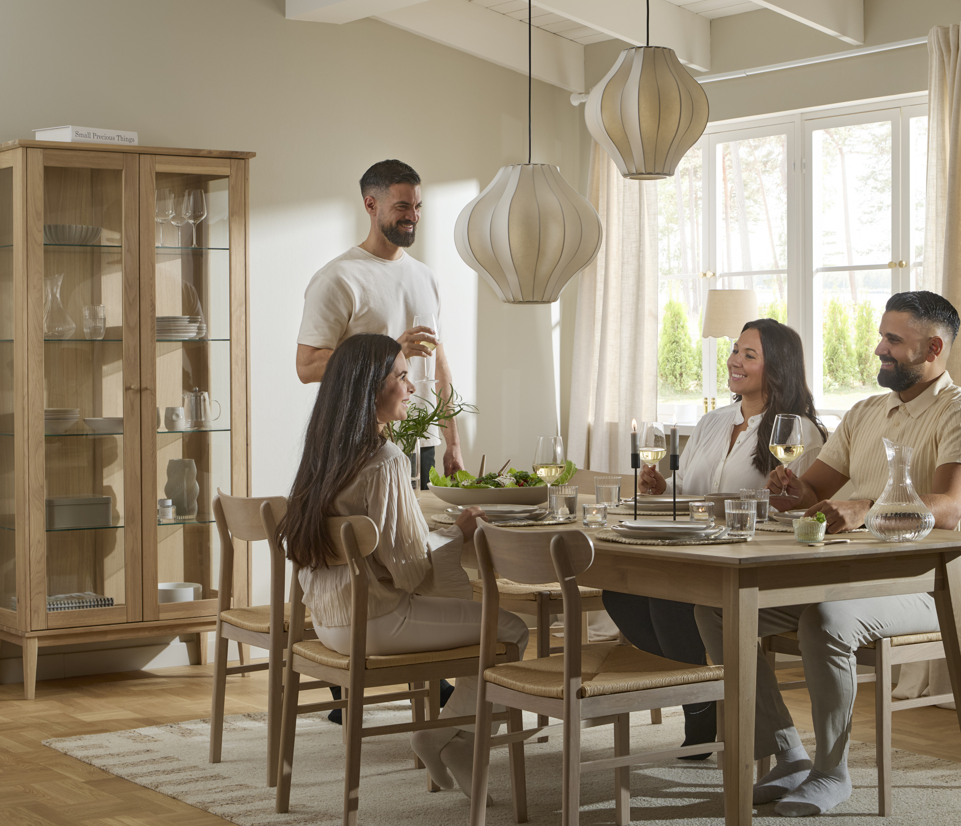 Fyra personer umgås kring ett matbord i ljust trä.