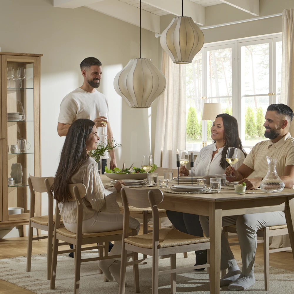 Fyra personer umgås kring ett matbord i ljust trä.