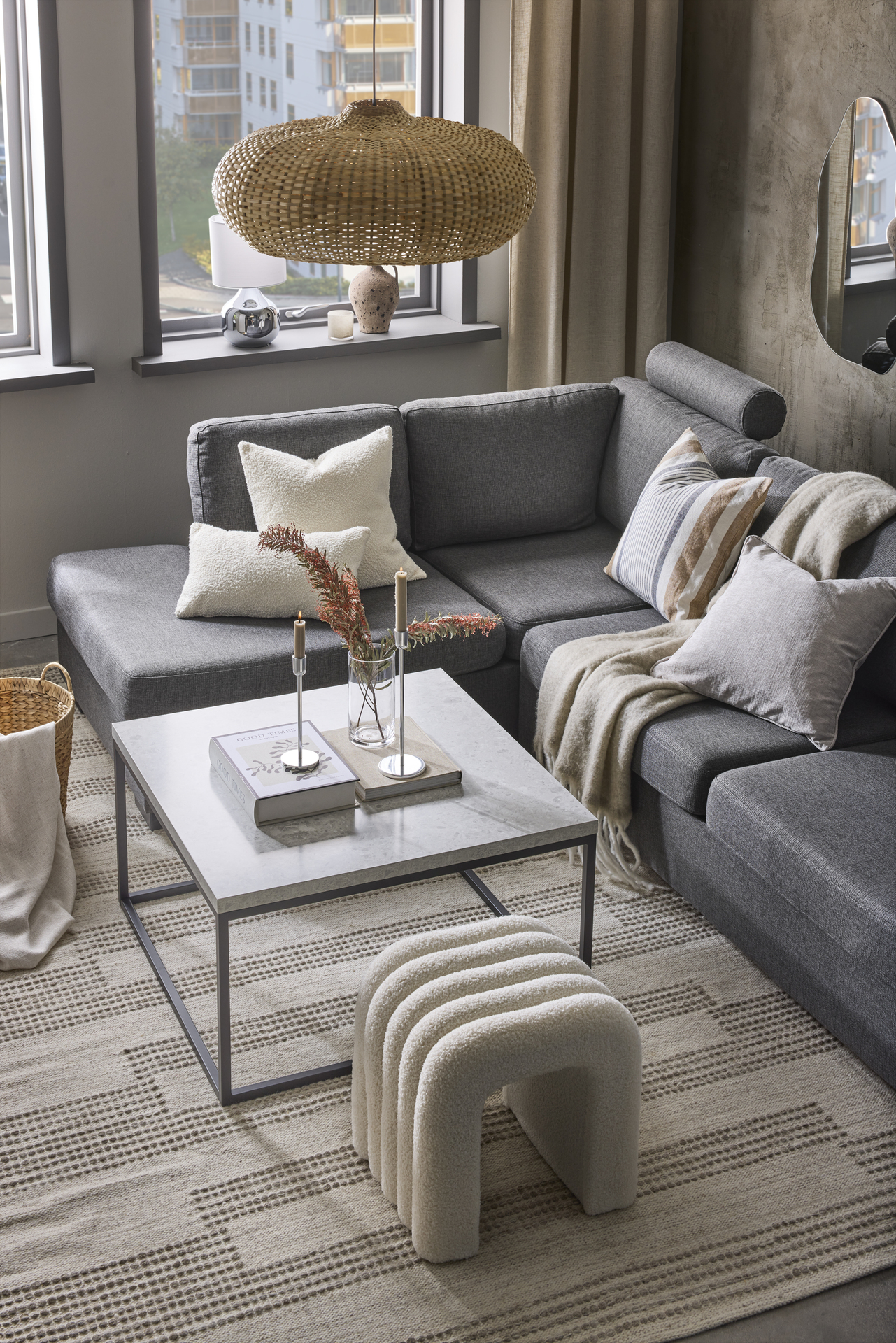 I ett stilrent vardagsrum står en grå divansoffa vid ett soffbord i sten