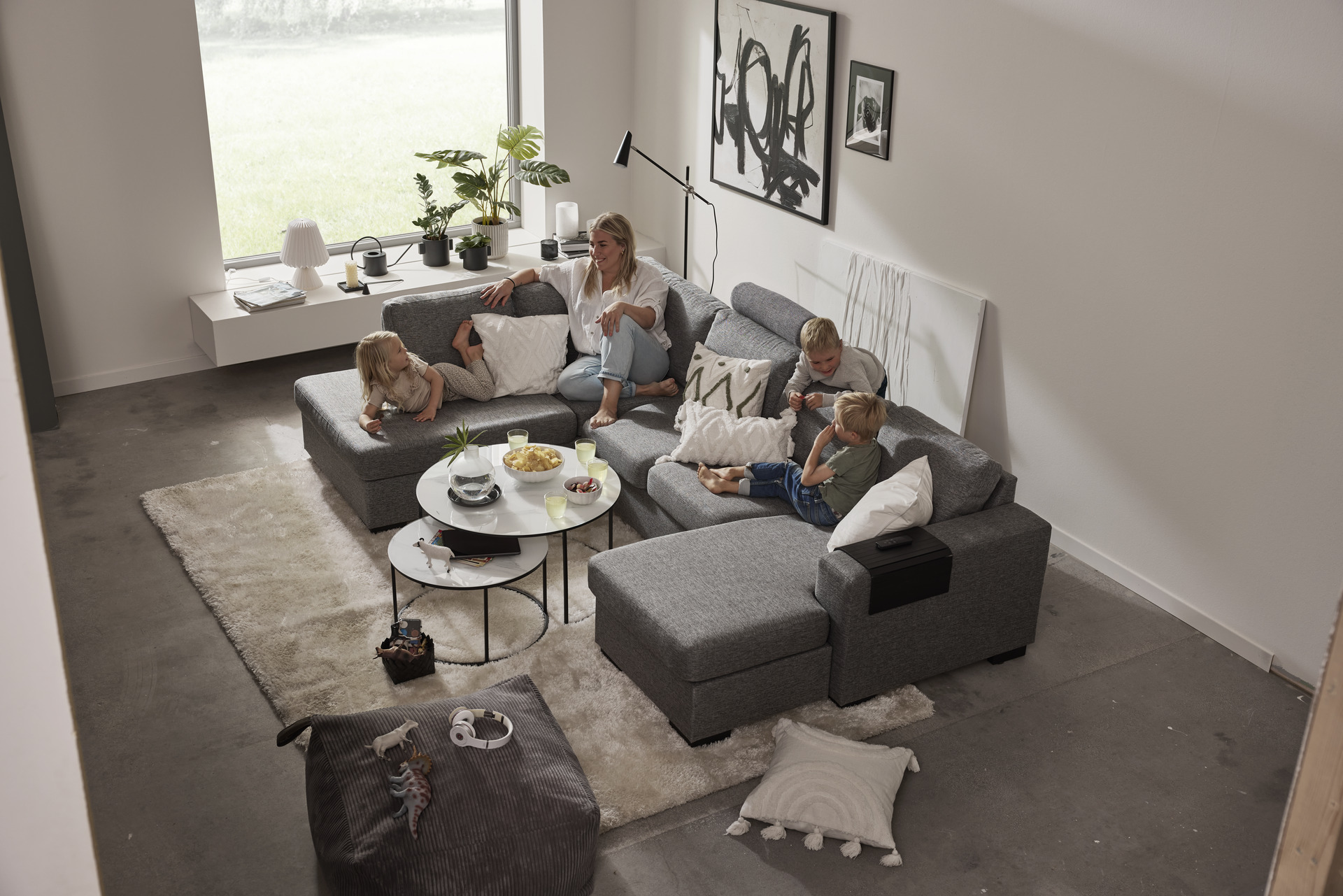 I en stor, grå soffa med både schäslong och divan sitter en kvinna och tre barn