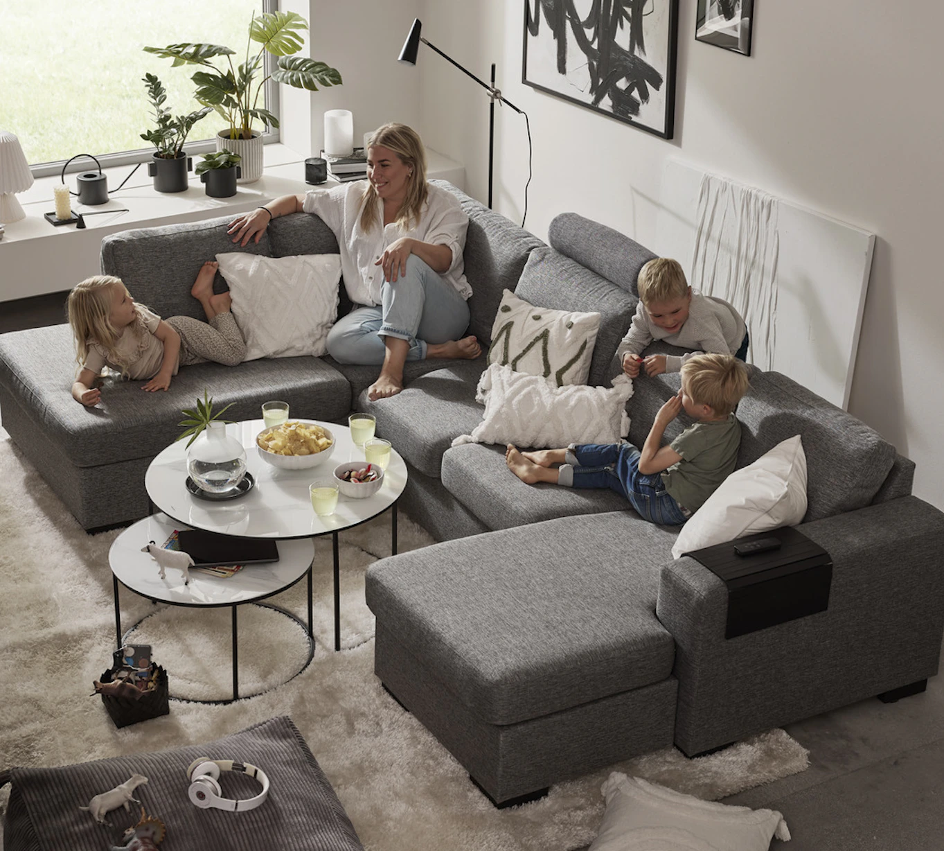 I en stor, grå soffa med både schäslong och divan sitter en kvinna och tre barn