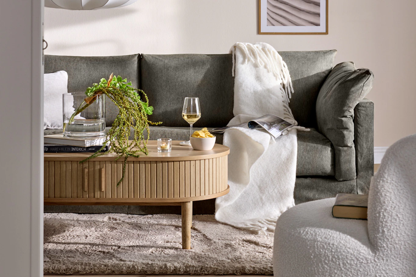 Vardagsrum med greige soffa, på soffbordet står ett vinglas och i soffan liger en pläd.