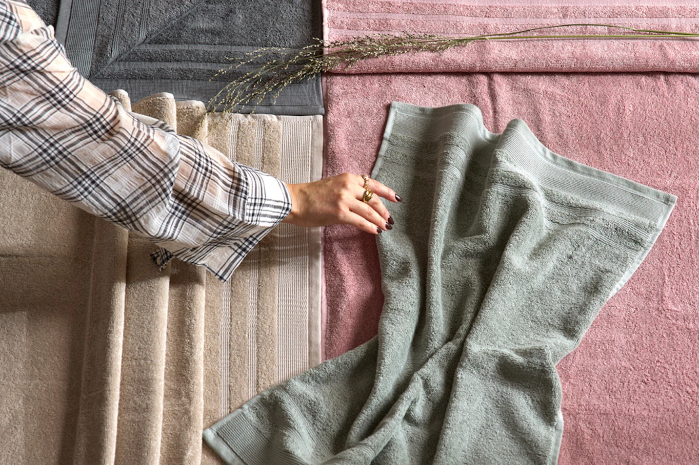 Hand sträcker sig efter en handduk på ett golv där flera handdukar i olika färger ligger. 