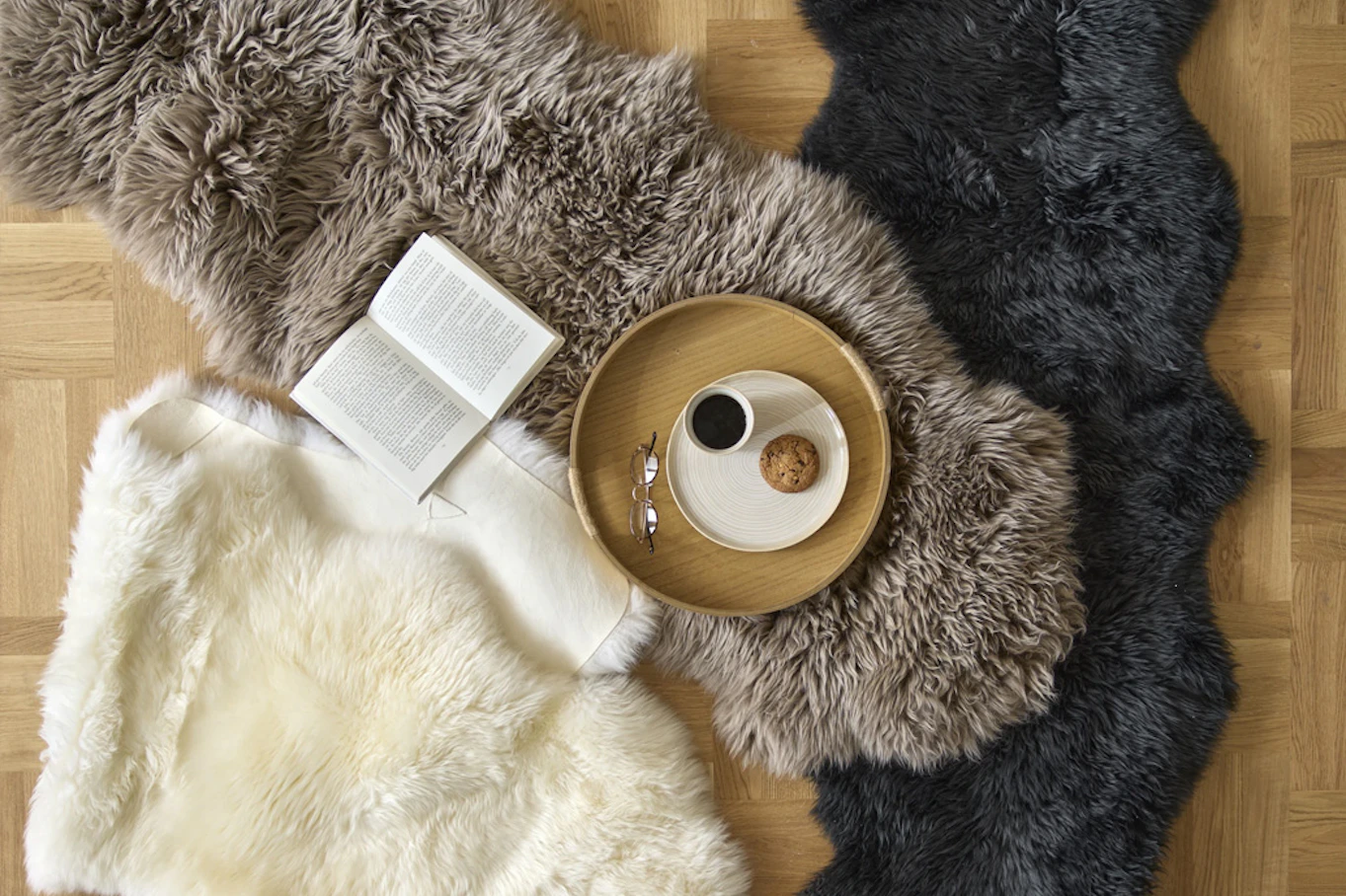 Fårskinn liggandes på golv, en bricka står på ena fårskinnet och en bok ligger uppvikt. 