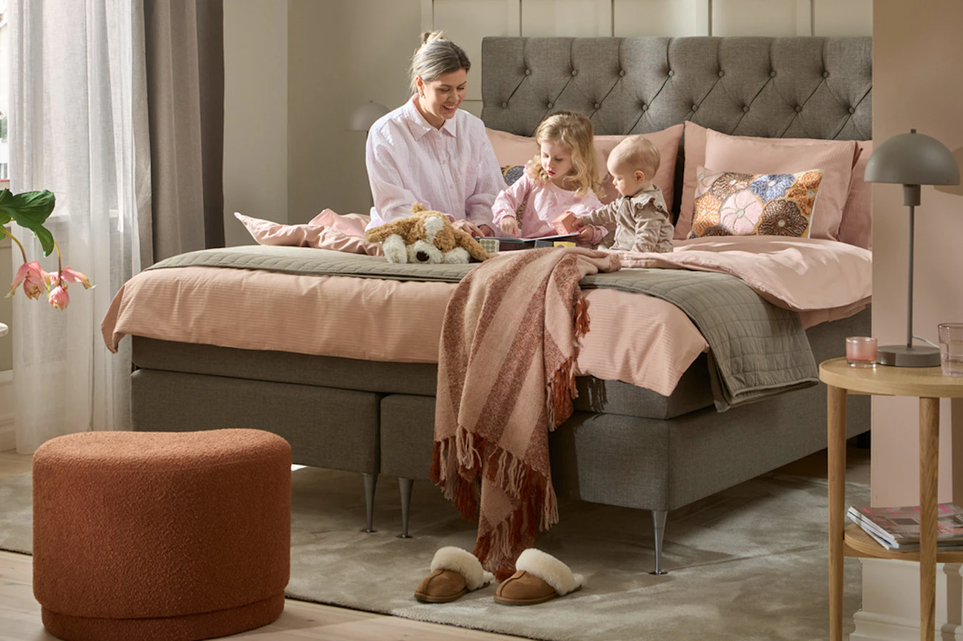 Kvinna sitter och leker med två små barn i en kontinentalsäng.