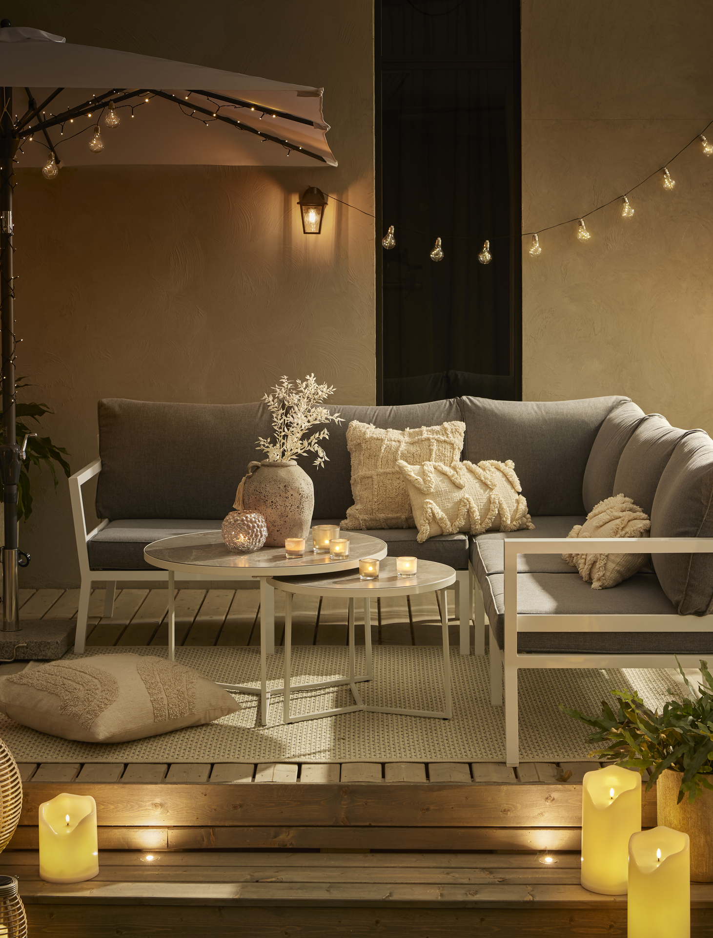 En hörnsoffa med runt satsbord står på ett trädäck dekorerat med ljusslingor och LED-ljus.