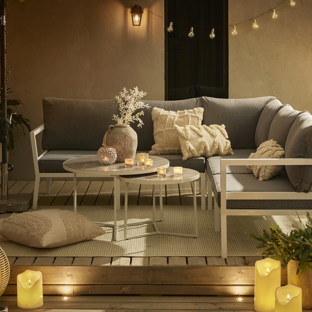 En hörnsoffa med runt satsbord står på ett trädäck dekorerat med ljusslingor och LED-ljus.