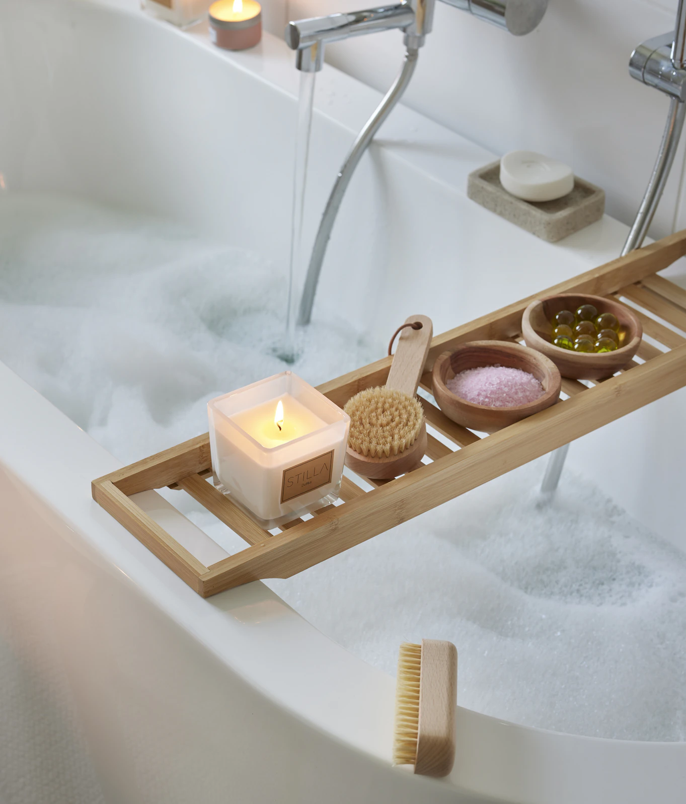 Badkarshylla över badkar med ett brinnande ljus och spadetaljer.