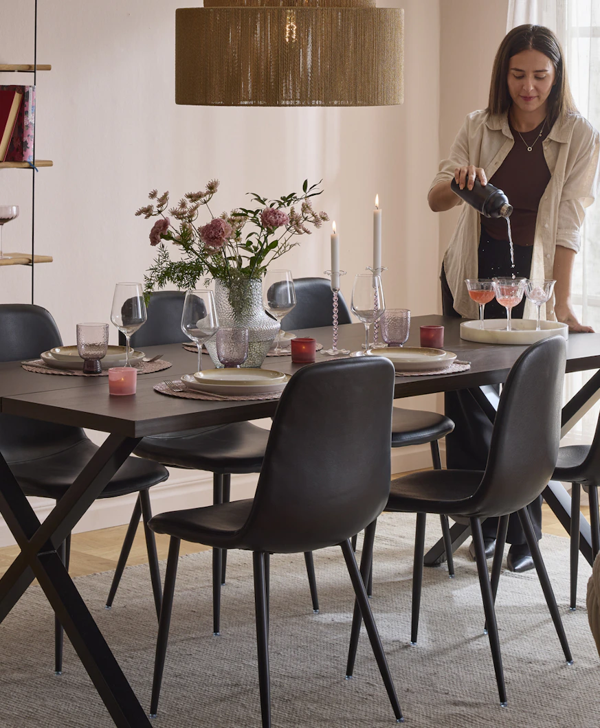 en tjej står och häller upp i glas vid en matgrupp i ett rum med rosa väggar