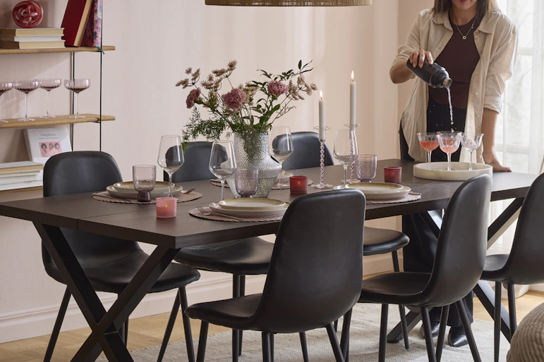 en tjej står och häller upp i glas vid en matgrupp i ett rum med rosa väggar