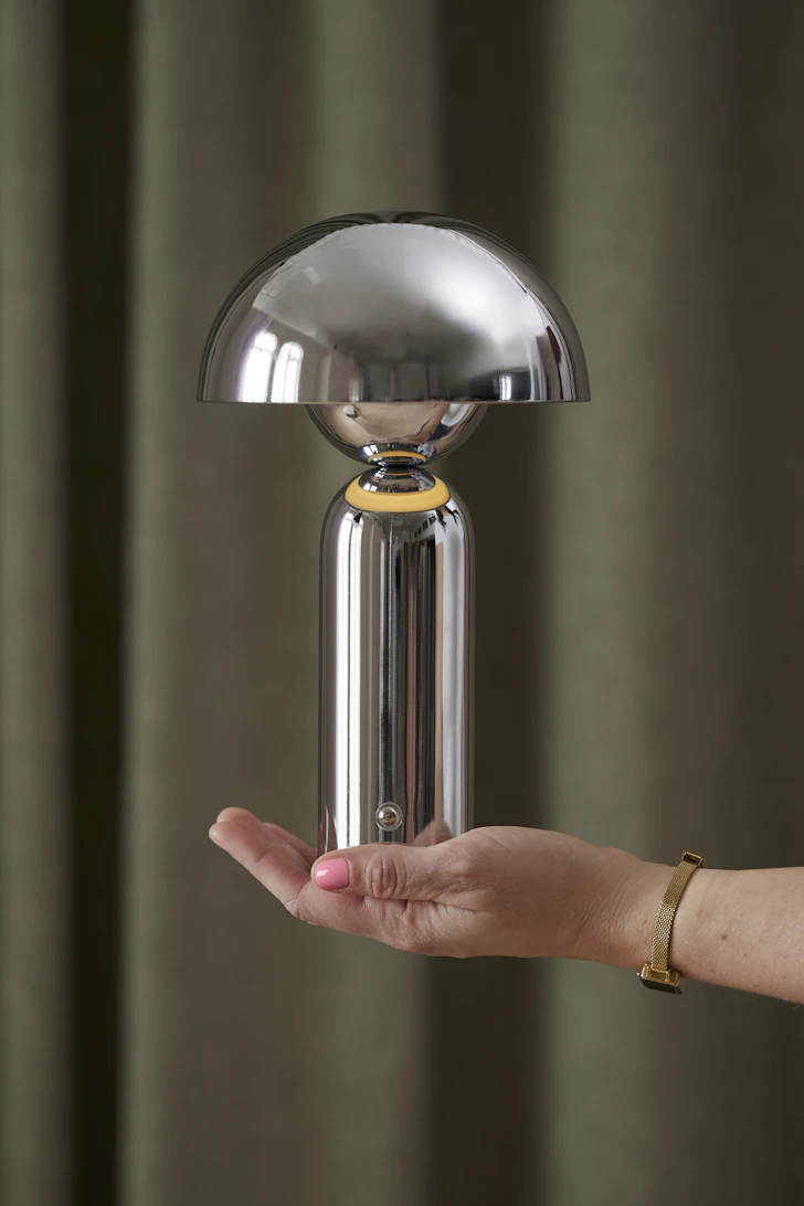 en hand som håller upp en portabel lampa i krom framför en grön bakgrund