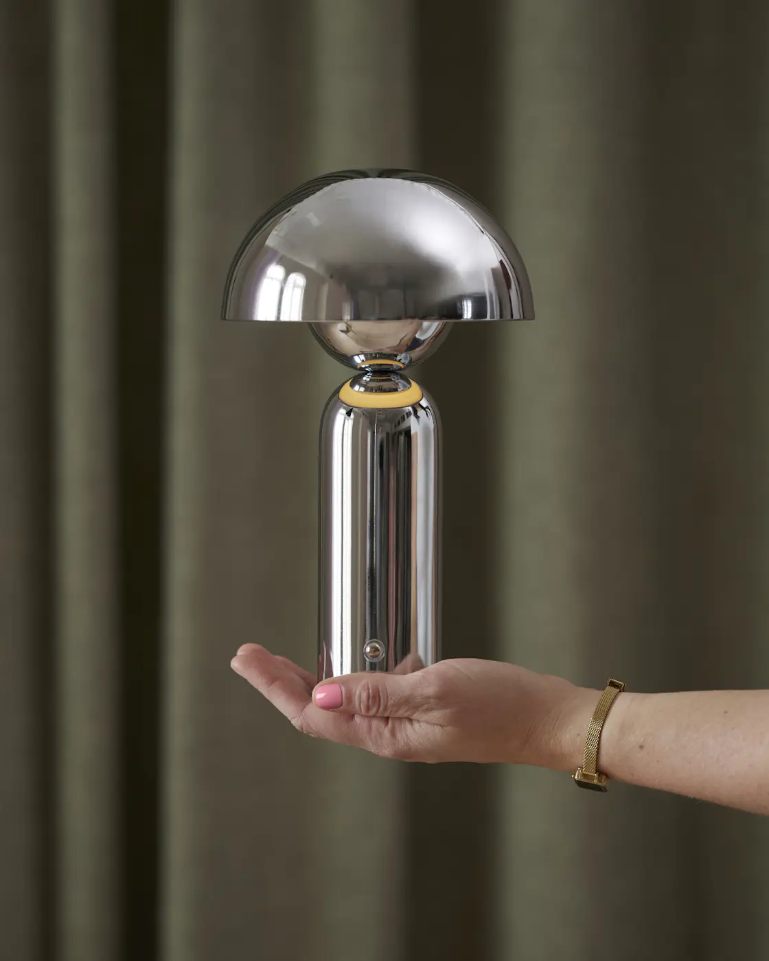 en hand som håller upp en portabel lampa i krom framför en grön bakgrund