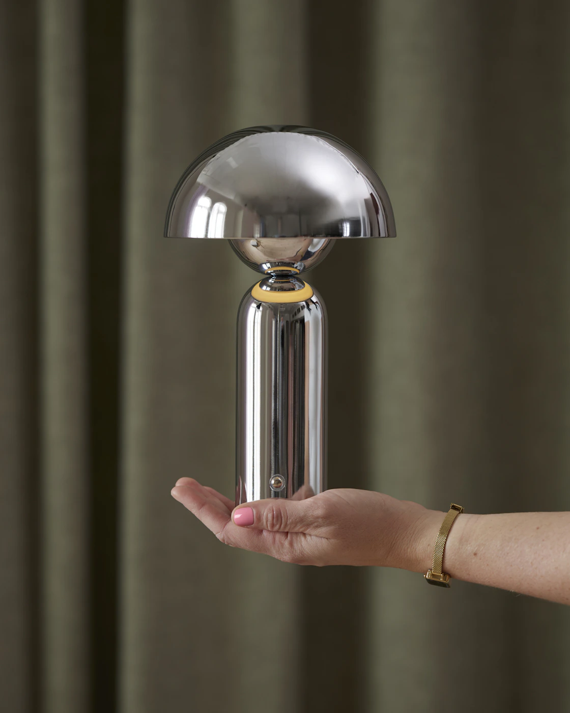 en hand som håller upp en portabel lampa i krom framför en grön bakgrund