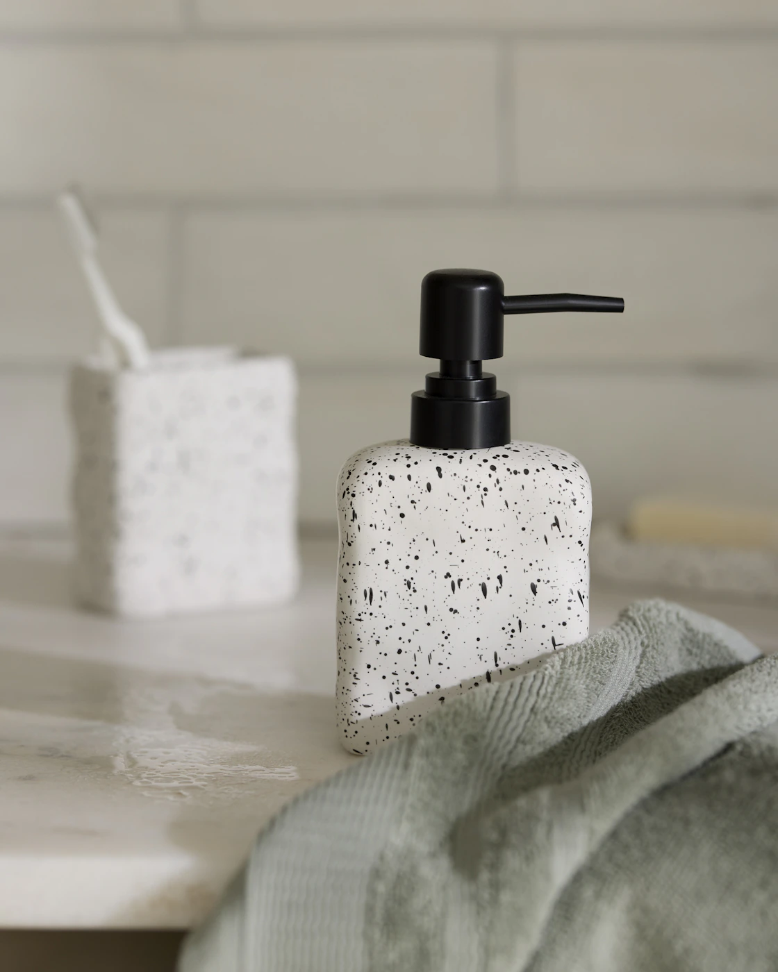 Vit tvålpumpe med svarta prickar på står på en hylla i badrum. 