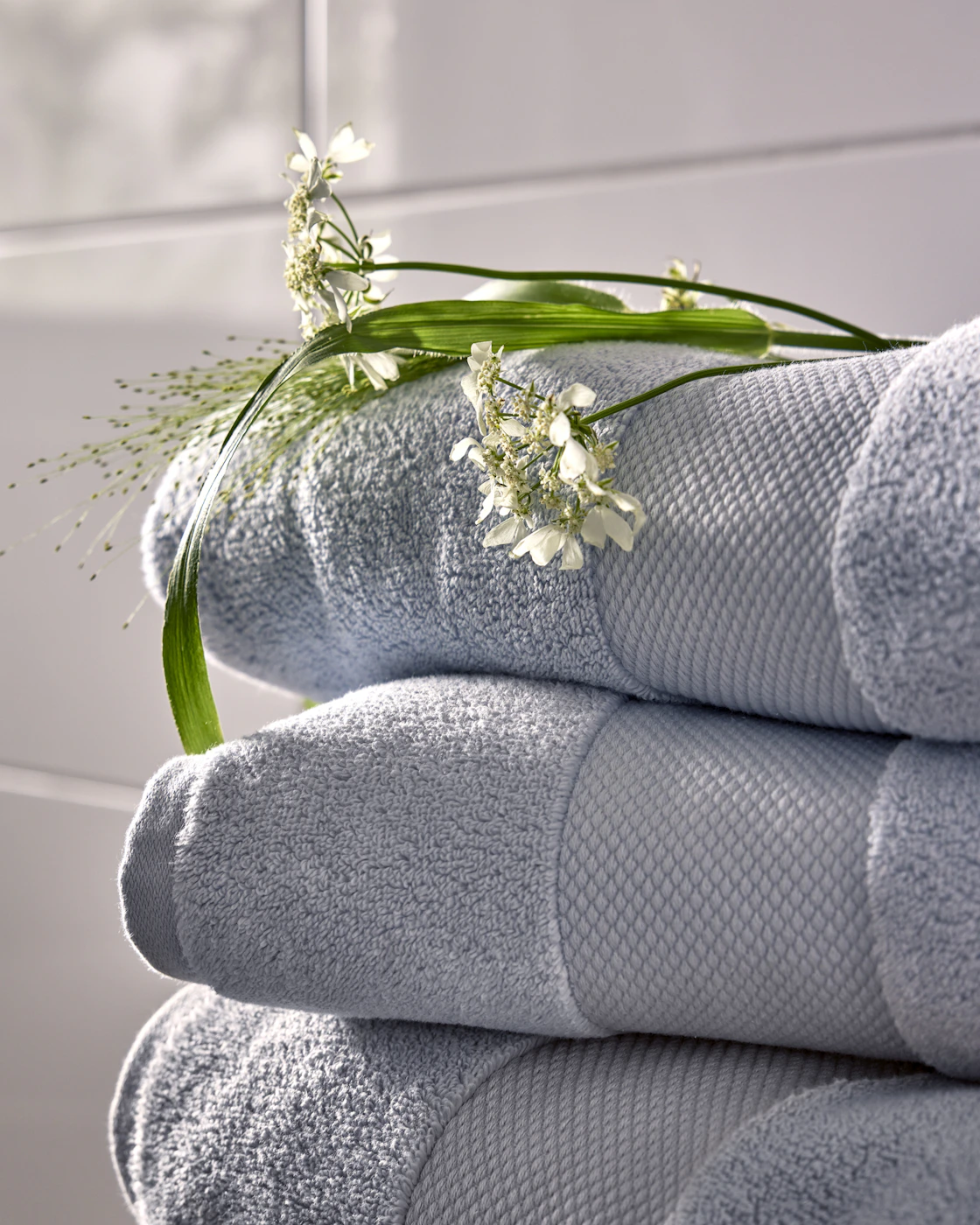 Hög med ljusblå fluffiga badlakan med en grön blomma och kvist liggandes ovanpå. 