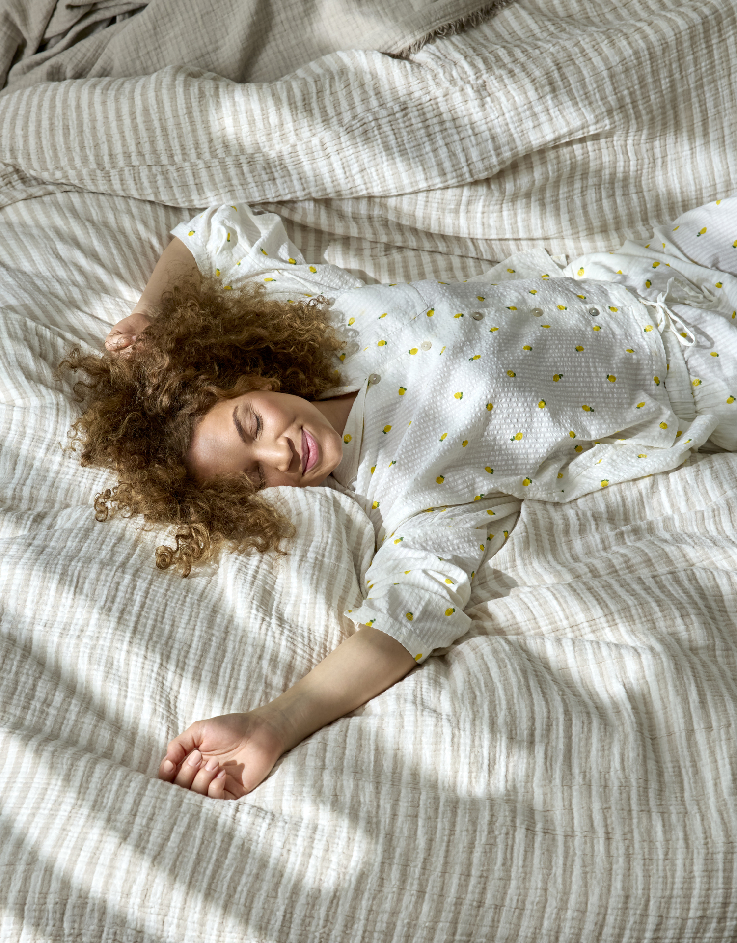 En kvinna i pyjamas med citroner på ligger utsträckt på rygg i en säng 