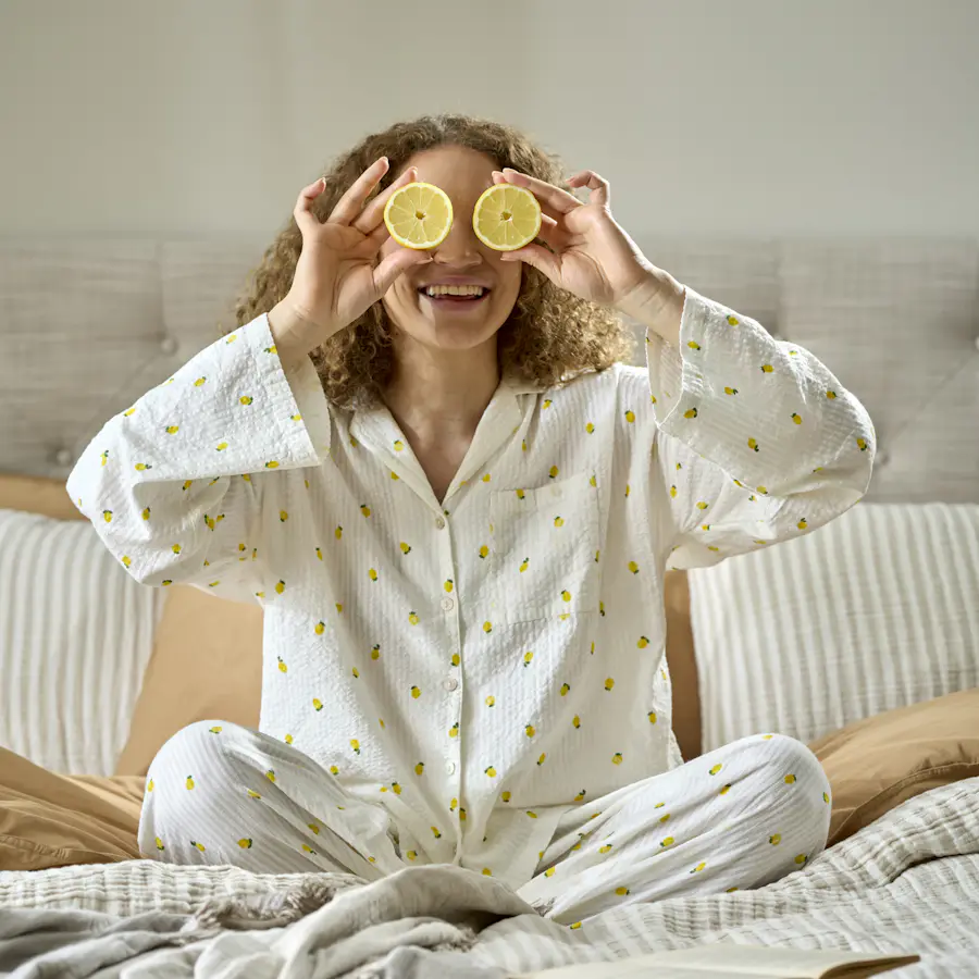 En kvinna i pyjamas sitter skräddare i en säng och håller två citronhalvor framför ögonen