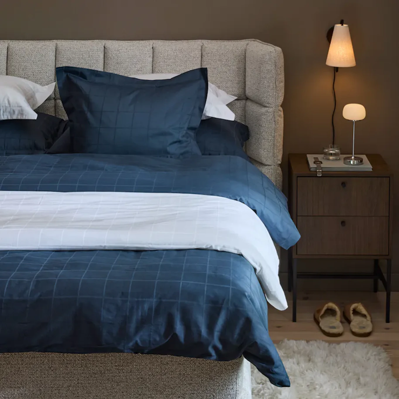 Sovrumsmiljö där halv säng syns med en rutad sänggavel som svängs ut från väggen.