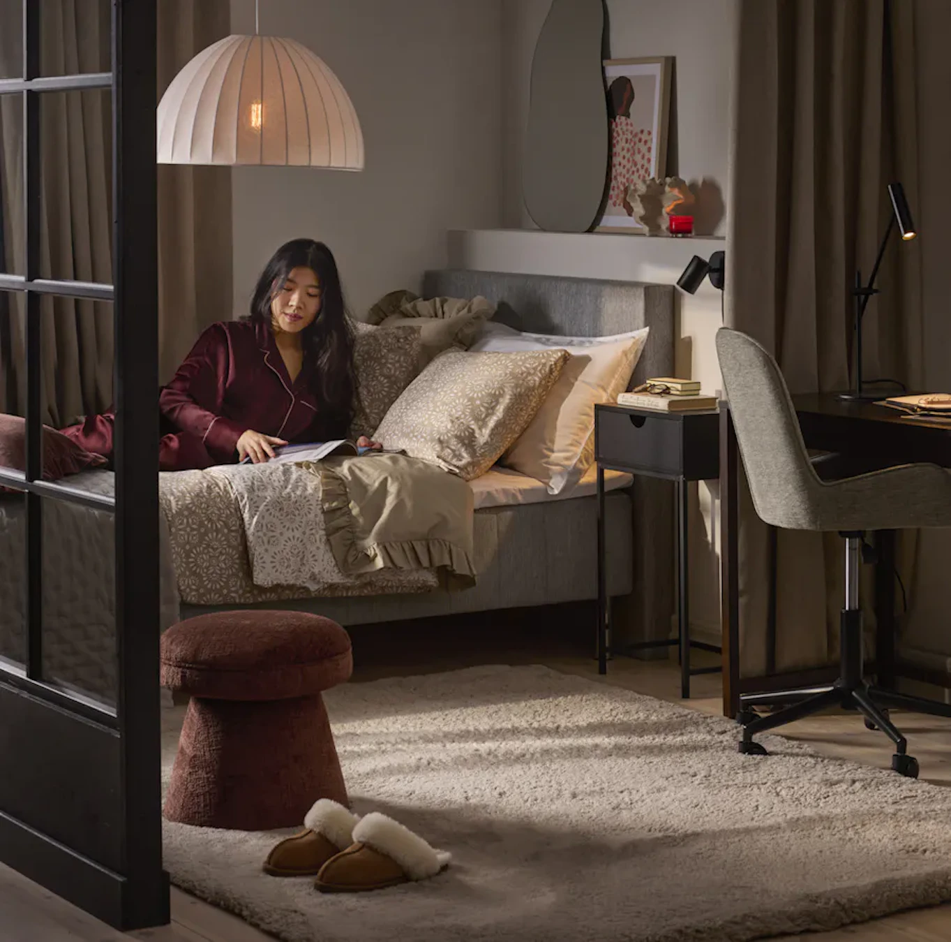 Kvinna halvligger i säng i ett mindre sovrum, i förgrunden står kontorsstol och skrivbord. 