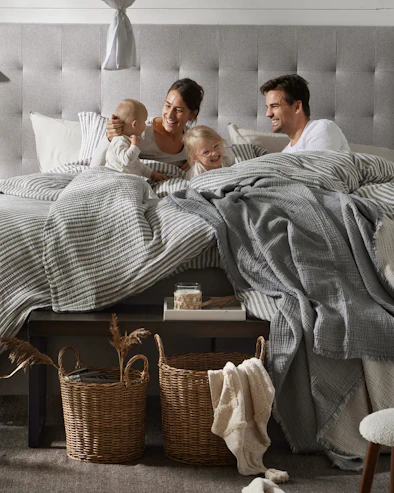 Barnfamilj med kvinna, man och två små barn ligger i kontinentalsäng och skrattar tillsammans.