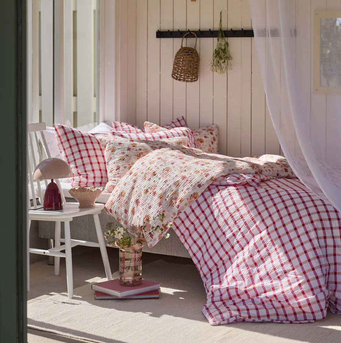 En säng står i solsken, bäddad med påslakan i blommigt och rutigt i rosa nyanser
