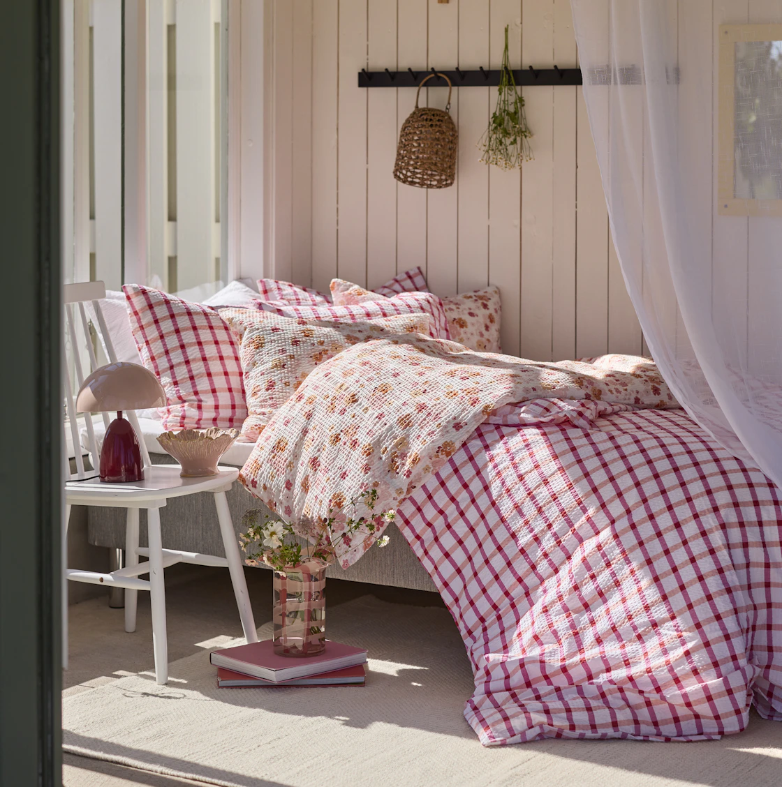 En säng står i solsken, bäddad med påslakan i blommigt och rutigt i rosa nyanser