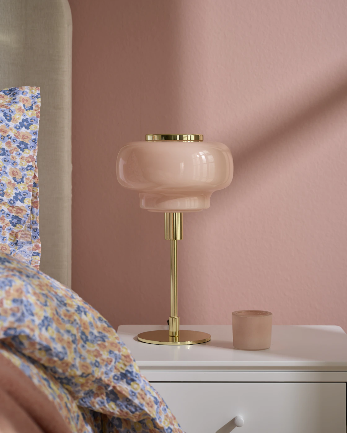 På ett nattduksbord står en rosa lampa med mässingfot