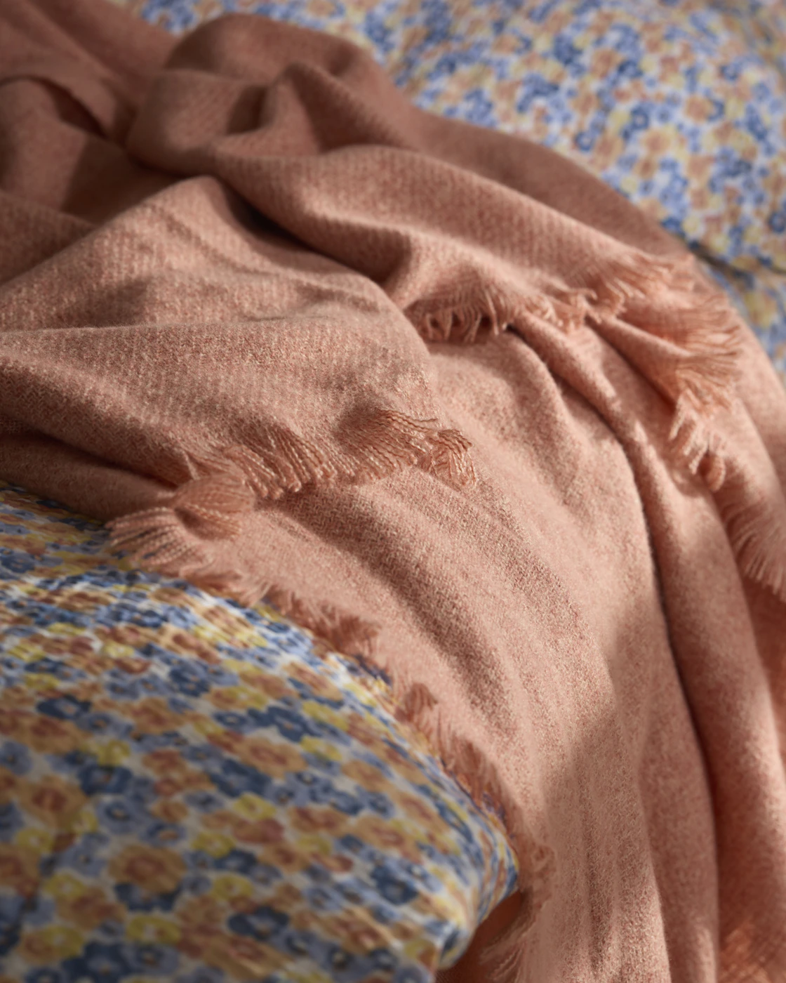 I en säng med ett blommigt påslakan i bäckebölja tyg ligger en korallfärgad filt