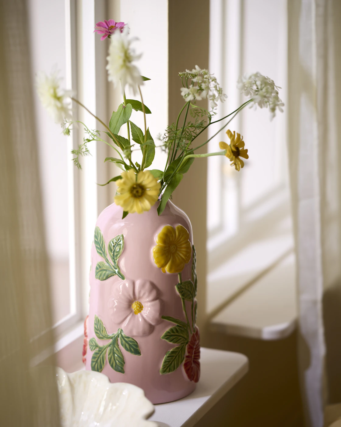 I ett fönster står en rosa vas med härliga blommor på, och i