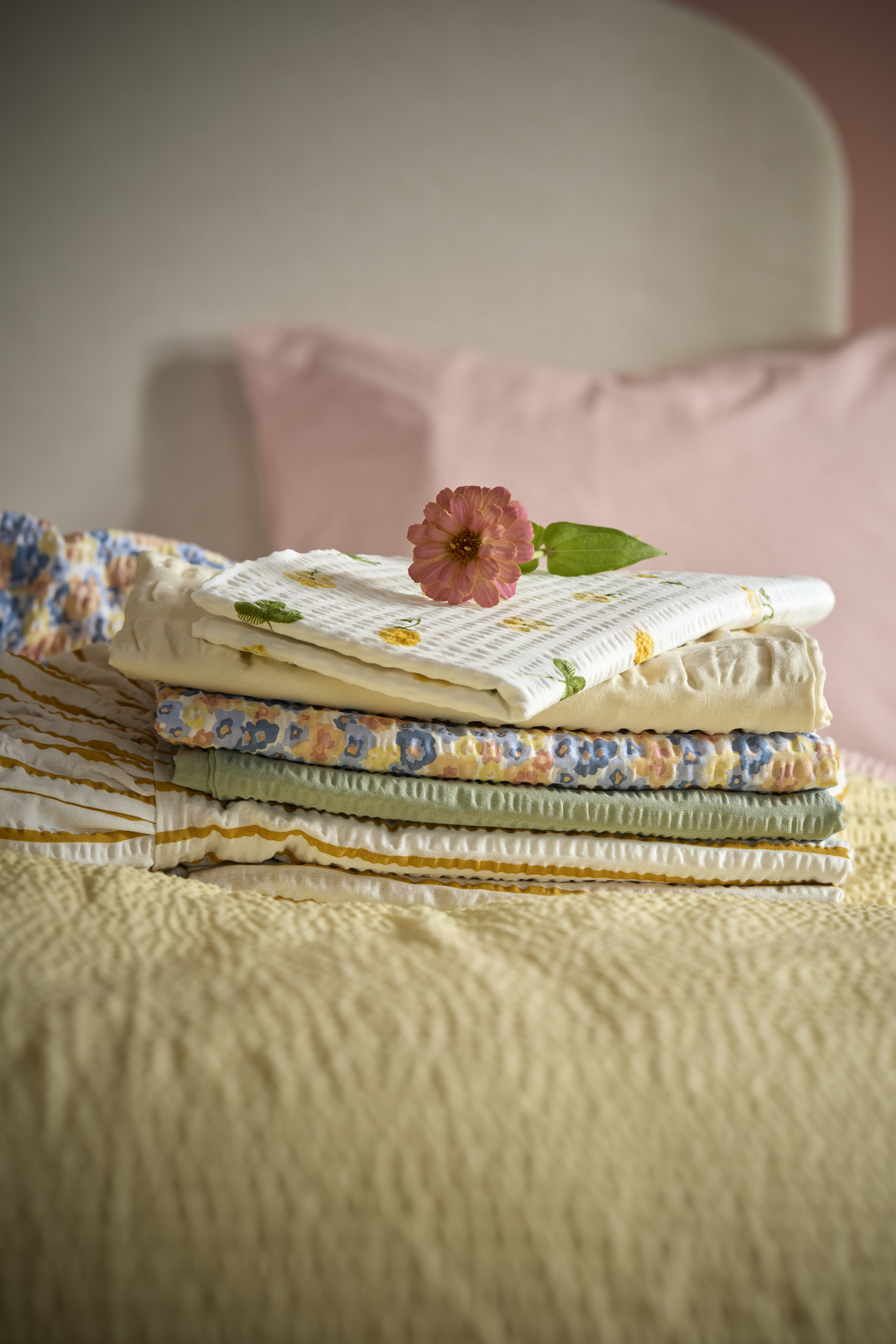 I en säng ligger en hög med örngott i våriga färger och mönster ihopvikta