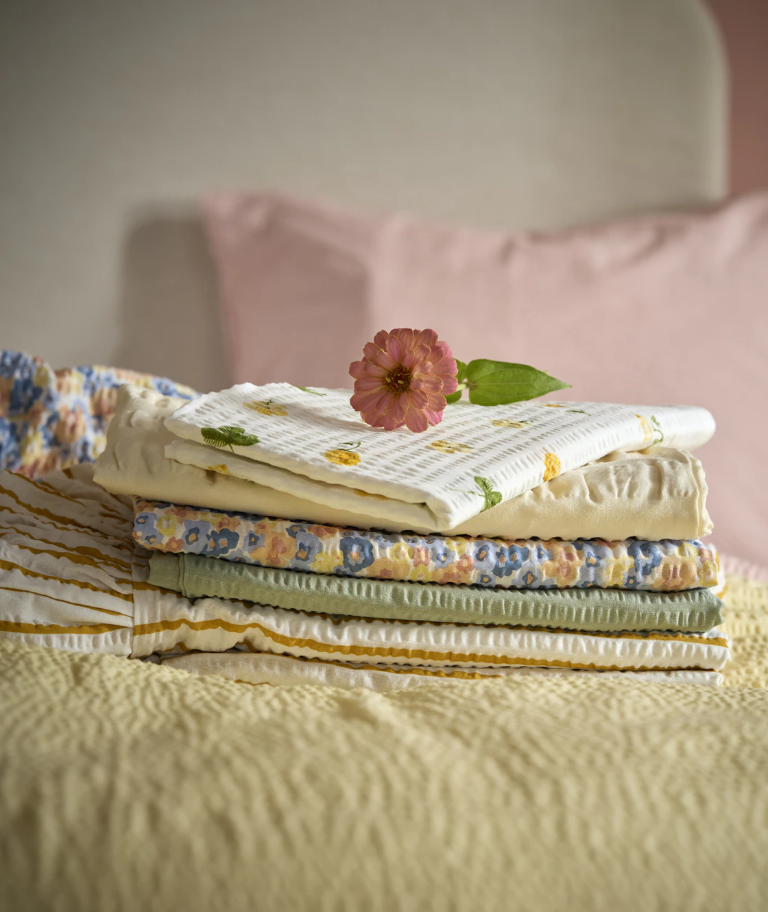 I en säng ligger en hög med örngott i våriga färger och mönster ihopvikta