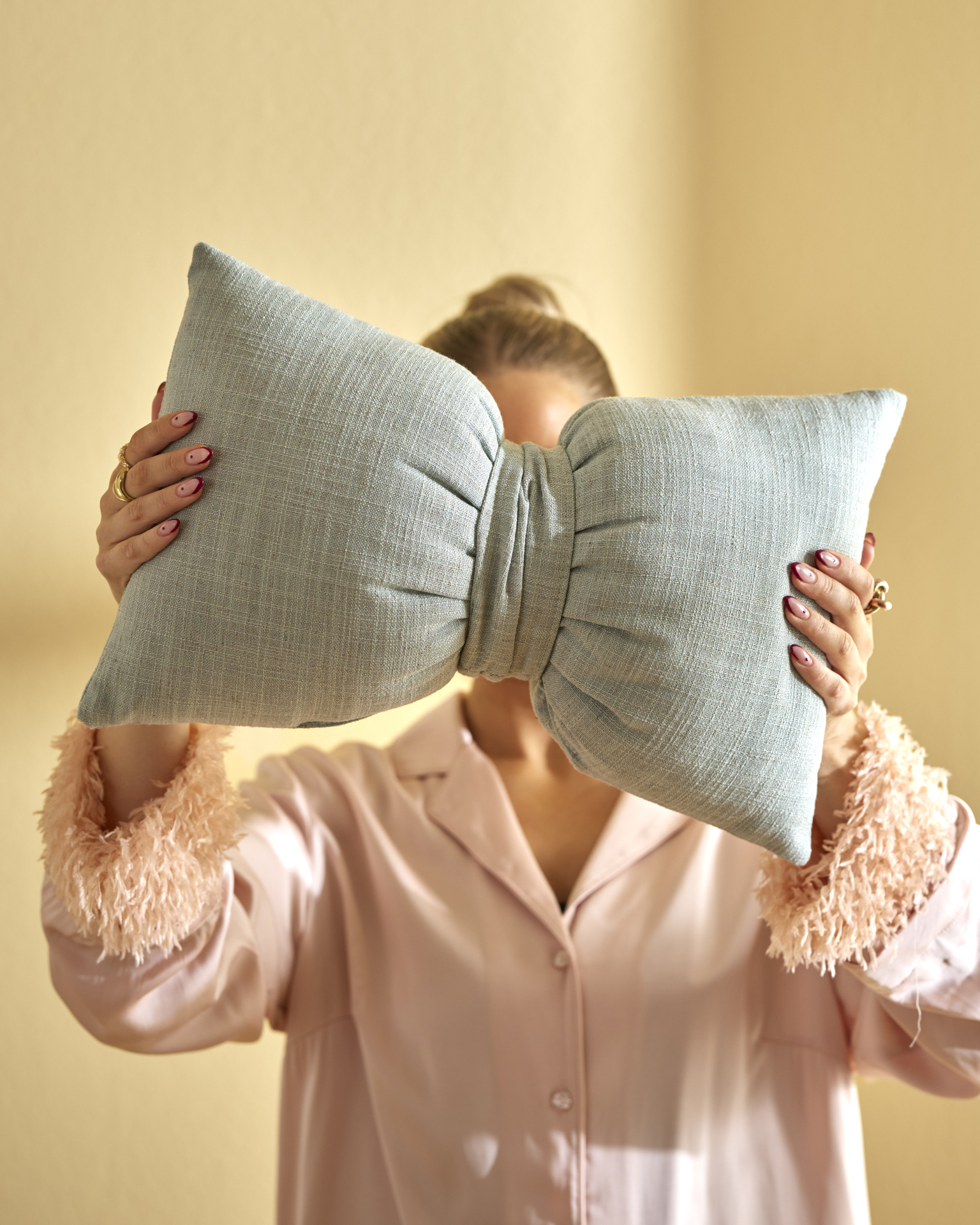 En kvinna står i ett gult rum och håller upp en grön kudde formad som en rosett framför ansiktet