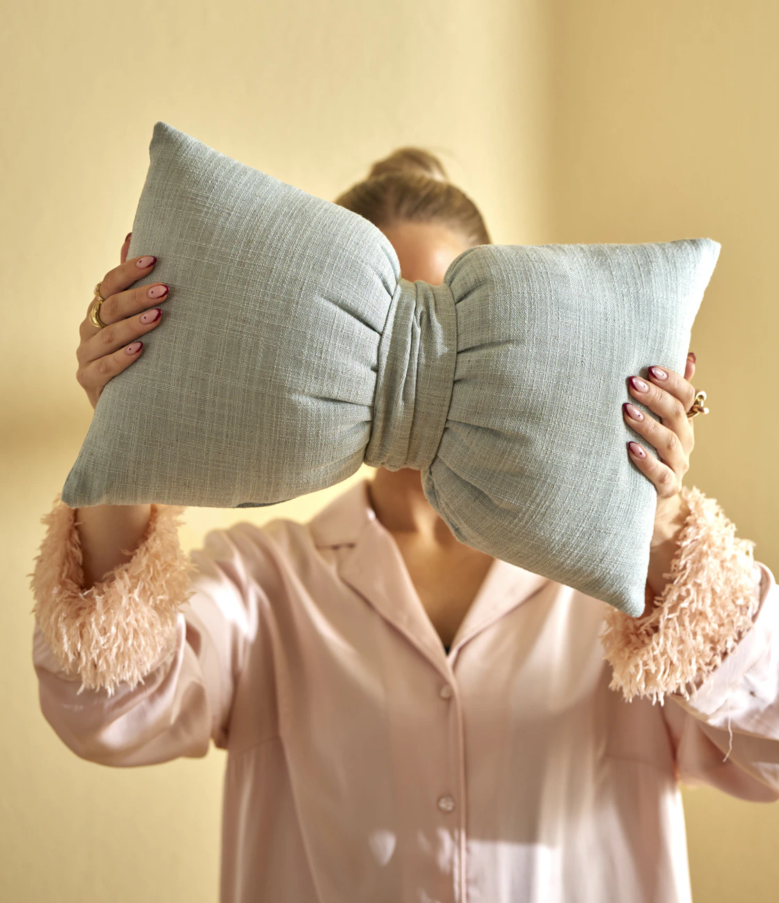 En kvinna står i ett gult rum och håller upp en grön kudde formad som en rosett framför ansiktet