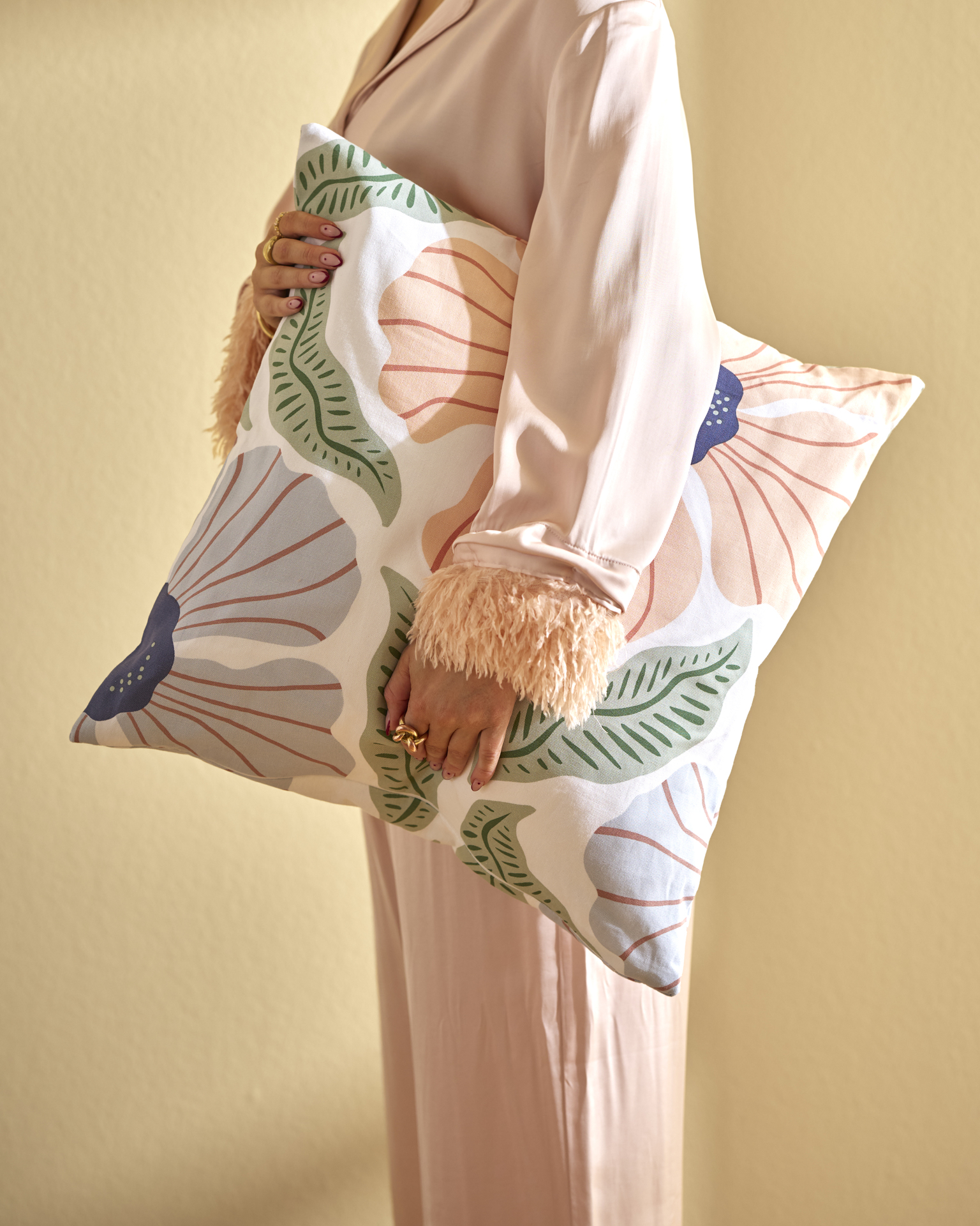 En kvinna håller i en kudde med storblommigt örngott i rosa, blått och grönt.