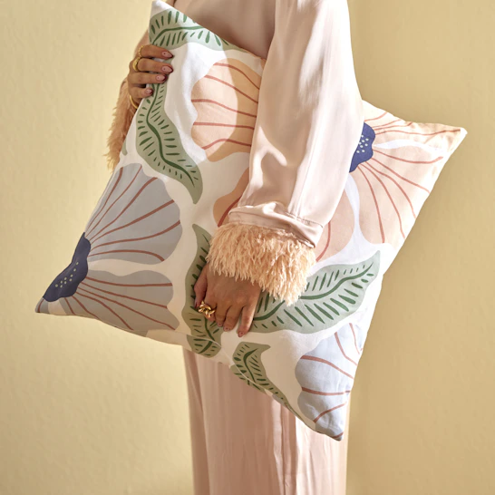 En kvinna håller i en kudde med storblommigt örngott i rosa, blått och grönt.