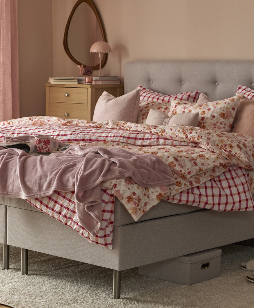 Säng med grå sänggavel och sängkläder i olika rosa och röda mönster.