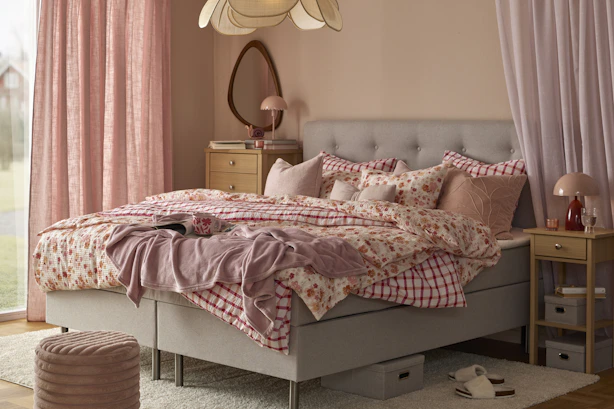 en grå säng bäddad med rosa påslakan i olika mönster står i ett sovrum
