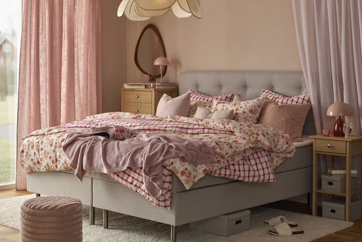 en grå säng bäddad med rosa påslakan i olika mönster står i ett sovrum