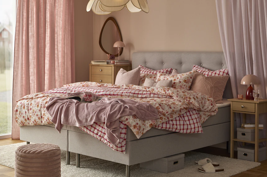 en grå säng bäddad med rosa påslakan i olika mönster står i ett sovrum