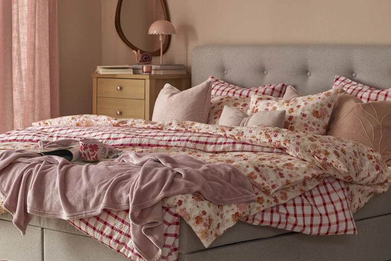 Säng med grå sänggavel och sängkläder i olika rosa och röda mönster.