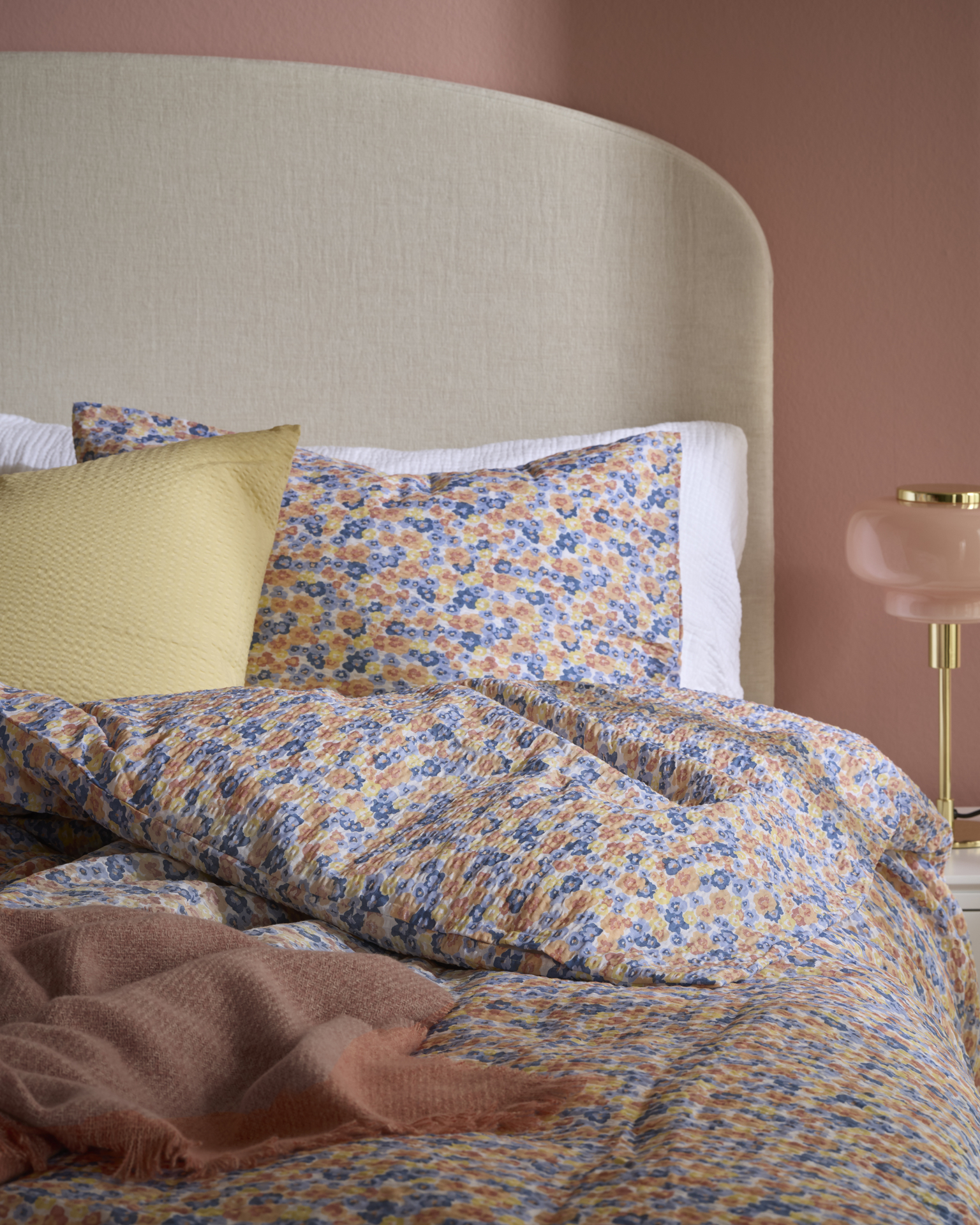 En säng är bäddad med småblommiga sängkläder i blått, gult och orange.