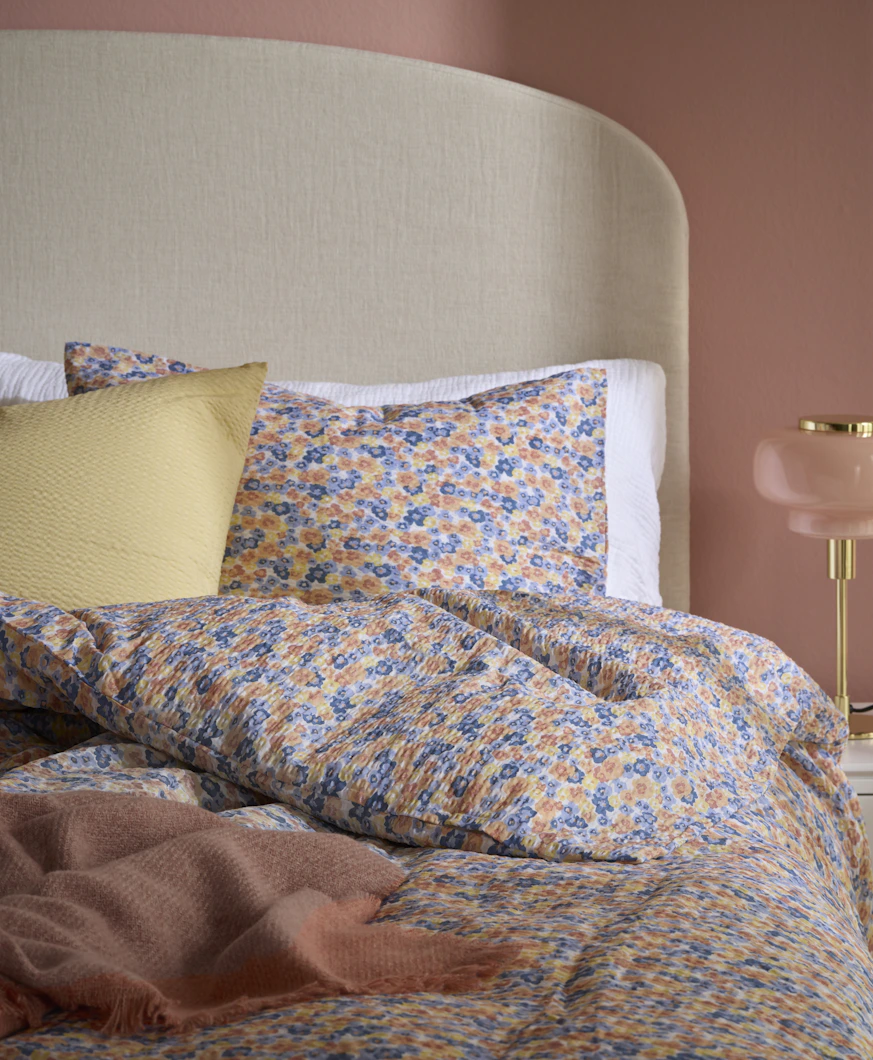 En säng är bäddad med småblommiga sängkläder i blått, gult och orange.