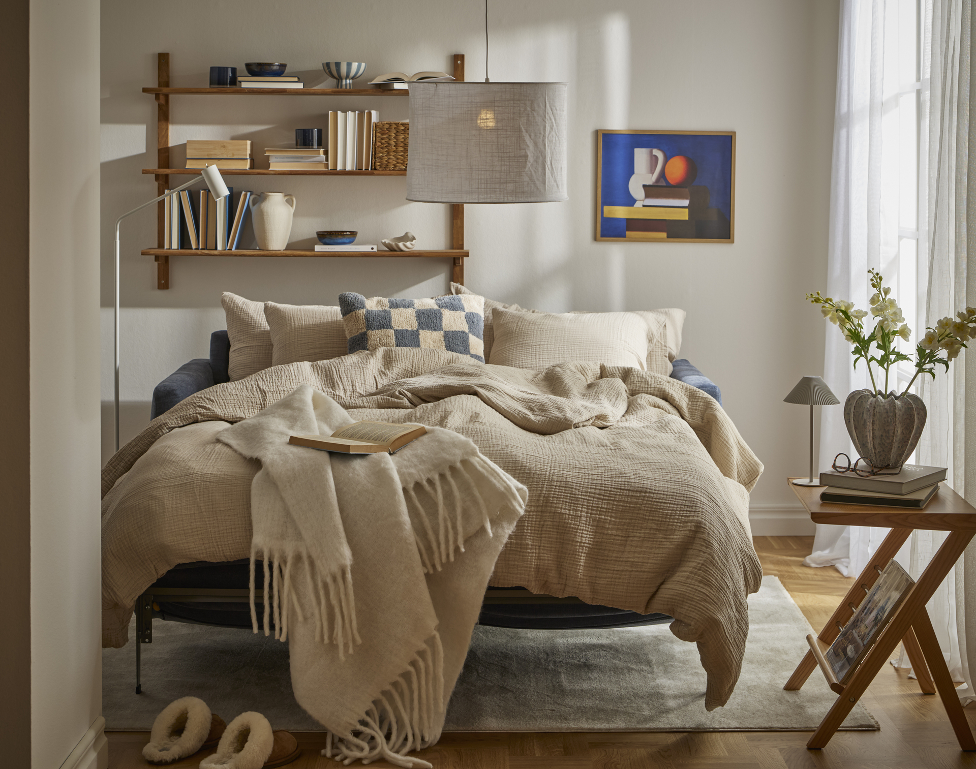 I ett ljust vardagsrum står en utfälld bäddsoffa med sängkläder i beige och blått.