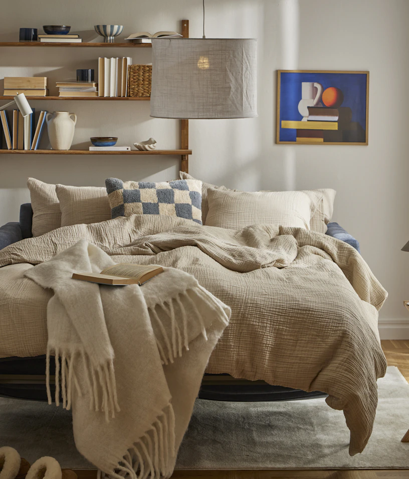 I ett ljust vardagsrum står en utfälld bäddsoffa med sängkläder i beige och blått.