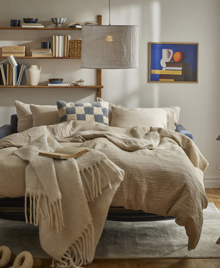 I ett ljust vardagsrum står en utfälld bäddsoffa med sängkläder i beige och blått.