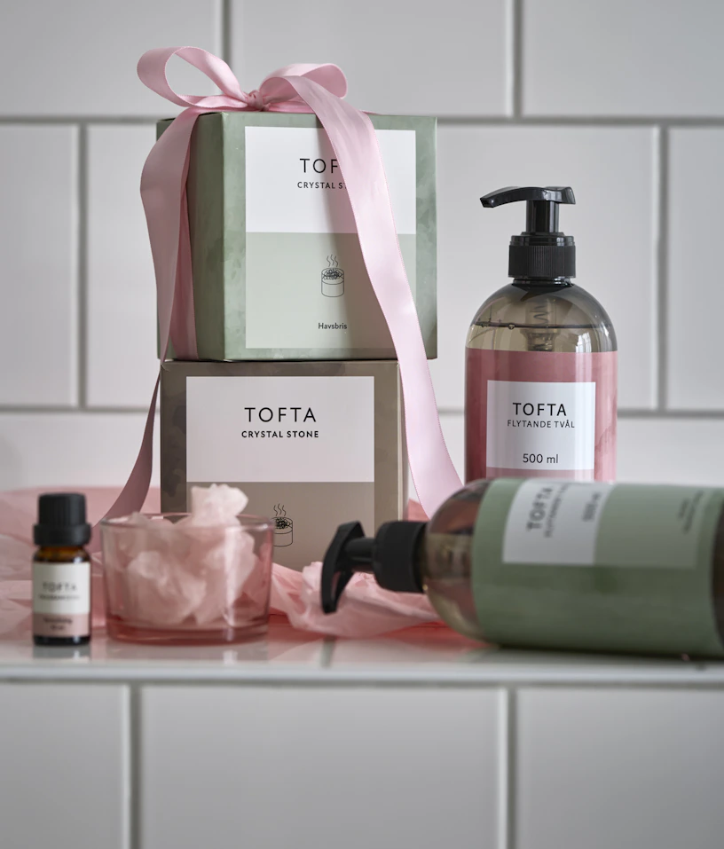 Paket med doftstenar omslagna med en rosa rosett och handtvål står framför en kaklad vägg.